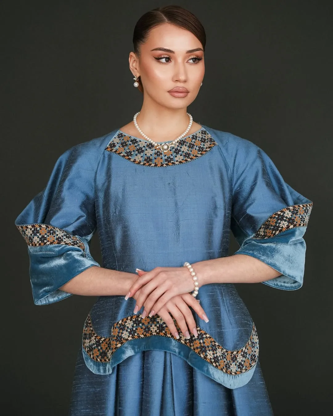 Studio portrait in blue silk — hands crossed, pearl accents
